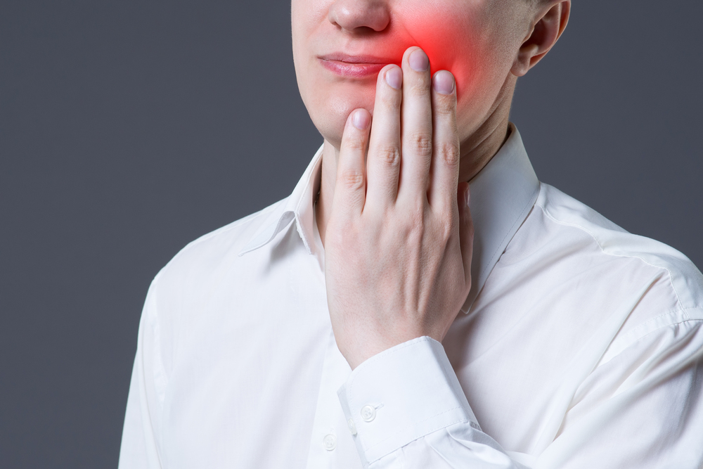 Man suffering from a toothache on gray background, painful area highlighted in red