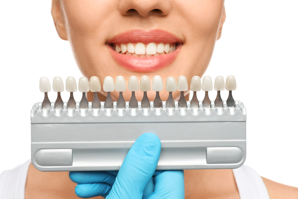 Doctor checking young woman's teeth color on white background, closeup. Cosmetic dentistry, veneers