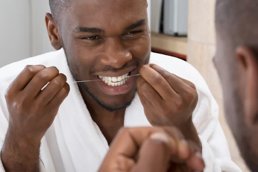 happy black man flossing his teeth wearing a white robe